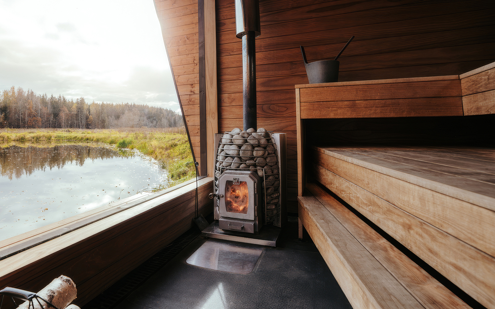 HUUM wood-fired sauna stove with flames visible through the glass door, set against cedar benching and a lake view